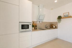 a white kitchen with white cabinets and a microwave at Villa Las Palmeras Valdevaqueros Suites, Pool & Sea Views in Tarifa +92 photos