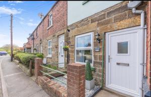 a brick house with a white door on a street at Ivydene Cottage Hawsker in Whitby