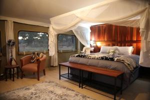 a bedroom with a canopy bed with a table and a chair at Chamabondo Luxury Tented Camp in Victoria Falls