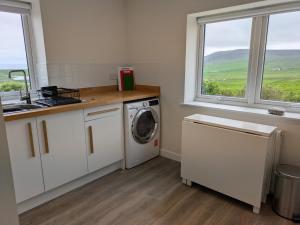 a kitchen with a washing machine and a sink and windows at Lower Cottage in Orkney