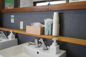 ein Waschbecken im Badezimmer mit Toilettenartikeln auf einem Regal darüber in der Unterkunft ゲストハウス ブランク Guest House BLANC in Hiroshima + 38 Fotos