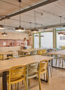 a man standing in a kitchen with tables and chairs at Hostelfly Fira Barcelona in Hospitalet de Llobregat