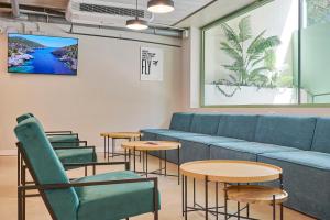 a waiting room with a blue couch and tables at Hostelfly Fira Barcelona in Hospitalet de Llobregat