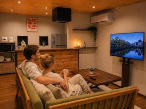 a man and woman sitting on a couch watching tv at TOMOSHIBI Kurashiki Zen House Near Bikan Historical Quarter 美観地区近く 和モダン一棟貸し in Kurashiki