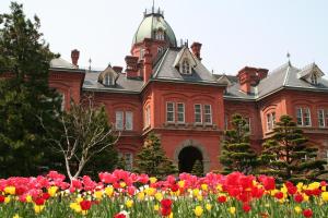 un gran edificio rojo con flores delante en Nest Hotel Sapporo Ekimae, en Sapporo