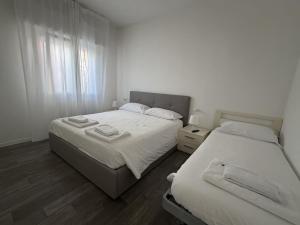 two beds in a bedroom with white walls and wood floors at Appartamenti Federica 12T in Milano Marittima