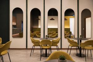 a restaurant with yellow chairs and tables and mirrors at LVG Hotel Collection - Belfiore in Mantova