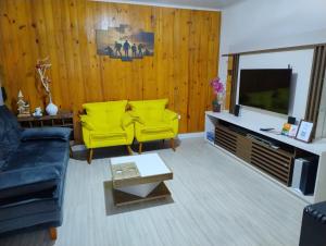 a living room with yellow chairs and a television at Hospedaria AlpenGlück in Treze Tílias