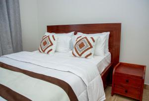 a bed with white sheets and pillows and a wooden headboard at Be Home Apartments in Nkoanrua