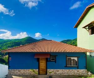 a blue house with mountains in the background at Morada Iluminada Aconchego com Ar condicionado e Lareira in Miguel Pereira