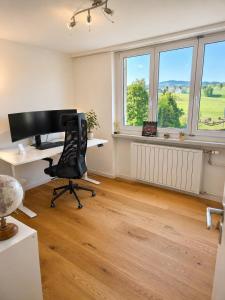 an office with a desk and a chair and windows at Stylish house with garden, sauna & pool in Mörschwil