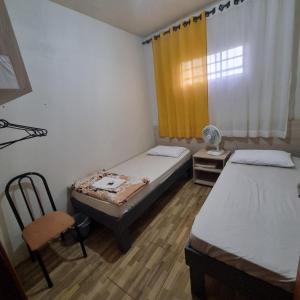 a room with two beds and a chair and a window at Hotel Do Parque in Ijuí