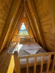a bed in a wooden room with a window at Alpine Cabins Gjinar in Gjinar