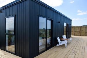 a black house with two white chairs on a deck at Tūhua View Retreat in Waihi Beach