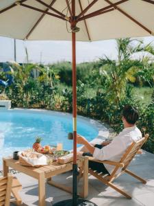 a man sitting in a chair under an umbrella by a pool at semilla 名護 沖縄 in Nago