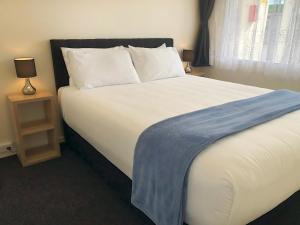 a bedroom with a large bed with a blue blanket on it at Twin Coast Adventures Motel & Cycle Hire in Kaikohe