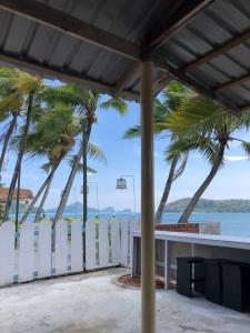 a white fence with palm trees in front of the water at Surf house langkawi in Pulau Tepur