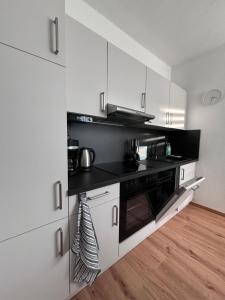 eine Küche mit weißen Schränken und einem schwarzen Herd mit Backofen in der Unterkunft Apartment 45 - Moderne, ruhige 2 Zimmer-Wohnung mit WLAN in Wittenberge, Komplett ausgestattet mit EBK, ideal für Business, Privataufenthalte, Radfahrer sowie kurze und längere Aufenthalte - einzeln oder als Paar - Nahe Bahnhof, Zentrum - Fahrradgarage in Wittenberge