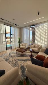 a living room with couches and a table and windows at إستراحة نمارق in Al ‘Aqar