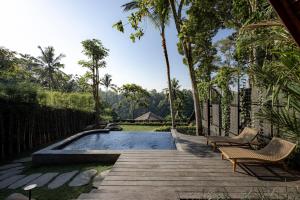a swimming pool with two chairs on a wooden deck at Bumi Kabins Ubud in Tegalalang