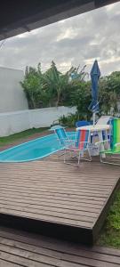 a deck with chairs and an umbrella next to a swimming pool at QUARTO AZUL com cozinha e piscina só sua in Capão da Canoa