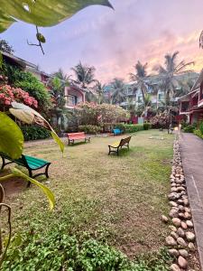 a park with benches and palm trees and houses at Subtlestays in Arpora