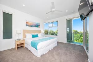 a white bedroom with a bed and windows at Akama Resort in Hervey Bay