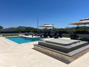 a swimming pool with chairs and umbrellas next to at Villa DEL SOLE with Heated Saltwater Pool, Jacuzzi and Sauna in Ljubuški