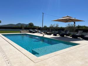 a swimming pool with chairs and an umbrella at Villa DEL SOLE with Heated Saltwater Pool, Jacuzzi and Sauna in Ljubuški