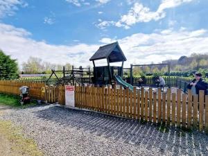 a playground behind a wooden fence with a slide at Twin Ayre Cabin Retreat Welshpool in Welshpool
