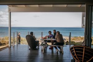 a group of people sitting at a table on a balcony with the ocean at Klipfontein House in Kleinbaai +39 photos