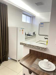 a white kitchen with a table and a refrigerator at Flat inteiro Ônix Bueno in Goiânia +192 photos
