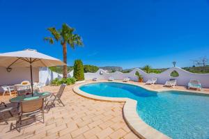a swimming pool with chairs and a table and an umbrella at Villa Mas Blanc - PlusHolidays in Benissa
