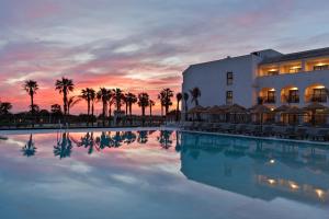 a resort with a pool and palm trees at sunset at Hotel Best Village Chipiona in Costa Ballena