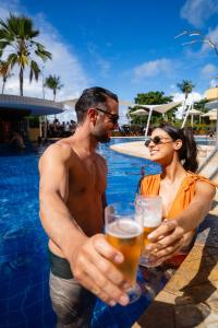 a man and woman holding glasses of beer by a swimming pool at Aquaria Natal Hotel in Natal