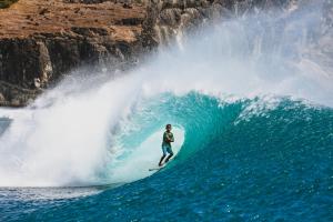 a man riding a wave on a surfboard in the ocean at Muara Surf House - Yoyos beachfront in Sekongkang