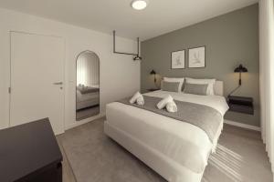 a white bedroom with a large bed and a mirror at Casa Jacinto 9 in Caldas da Rainha
