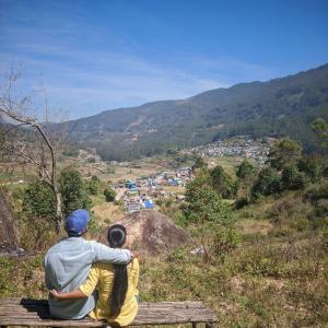a man and a boy sitting on a bench looking at a valley at Budget couple rooms vattavada in Vattavada