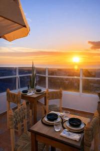 a table and chairs on a balcony with a sunset at Adrar Lodge - Boutique Guesthouse with Sea View in Tamraght Ouzdar