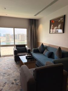a living room with blue couches and a large window at Mora by jodna - فندق مورا in Al Khobar