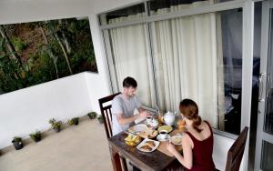 Ein Mann und eine Frau sitzen am Tisch und essen Essen. in der Unterkunft Sunray Homestay in Ella