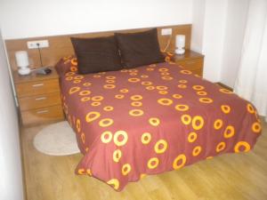 a bed with a red comforter with yellow flowers on it at Apartamento Ana Sebastián in Lorenzana