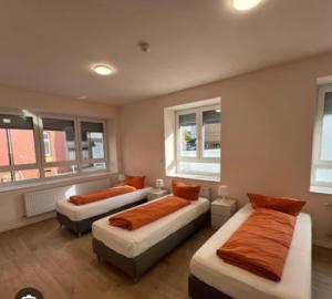 two beds with orange pillows in a room with windows at E&B Pension in Ganderkesee