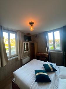 a bedroom with a bed with two pillows and two windows at Hotel Des Bains in Veulettes-sur-Mer