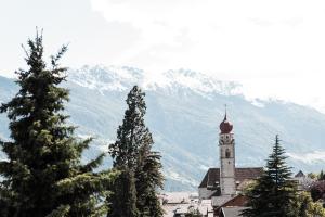 a church with a clock tower in front of a mountain at SIEGI apartments & retreat - Merano Südtirol in Parcines +61 photos