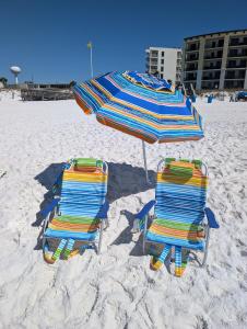 two beach chairs and an umbrella on the beach at Gulf Balcony - Boutique Comforts & 2 King Suites in Fort Walton Beach