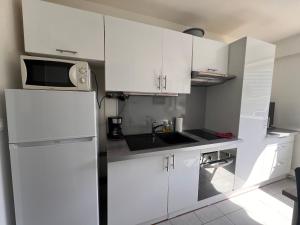 a kitchen with white cabinets and a sink and a microwave at La Studette Marina 06 in Villeneuve-Loubet