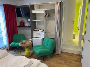 a bedroom with a bed and two green chairs and a table at Hotel De Backer in Knokke-Heist