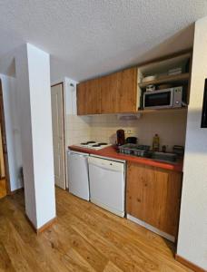 a small kitchen with white appliances and wooden cabinets at DFJ des Neiges, Piscine, Pieds des pistes in Chamrousse