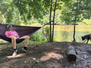 a woman sitting in a hammock next to a river at The Outside Inn in Cullowhee